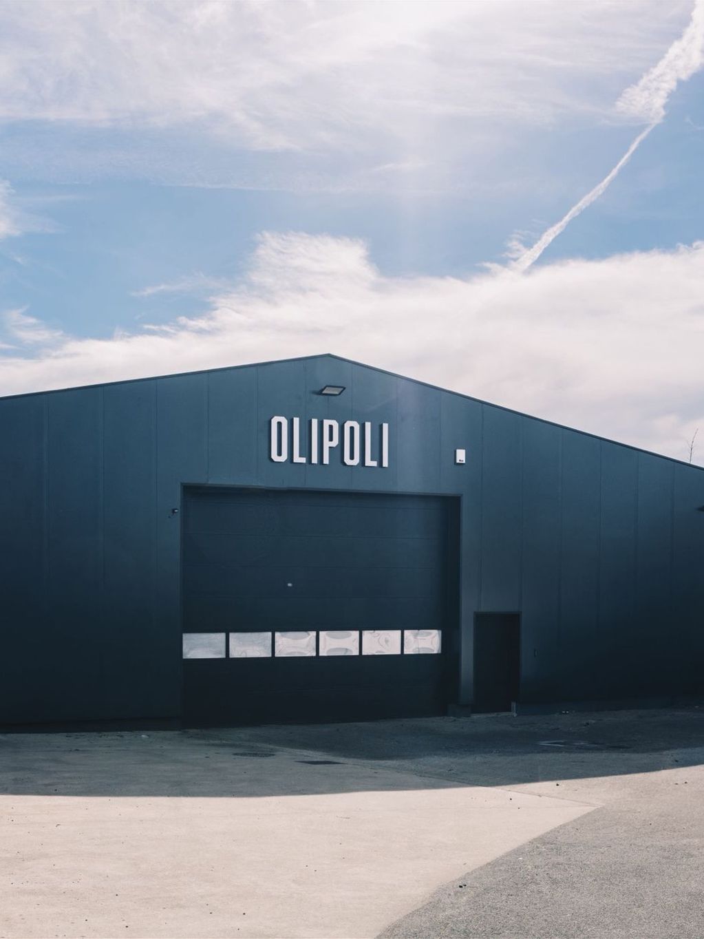De OliPoli-hal na de werken, recht van voren: een gevel in donkere sandwichpanelen rond poort en deur