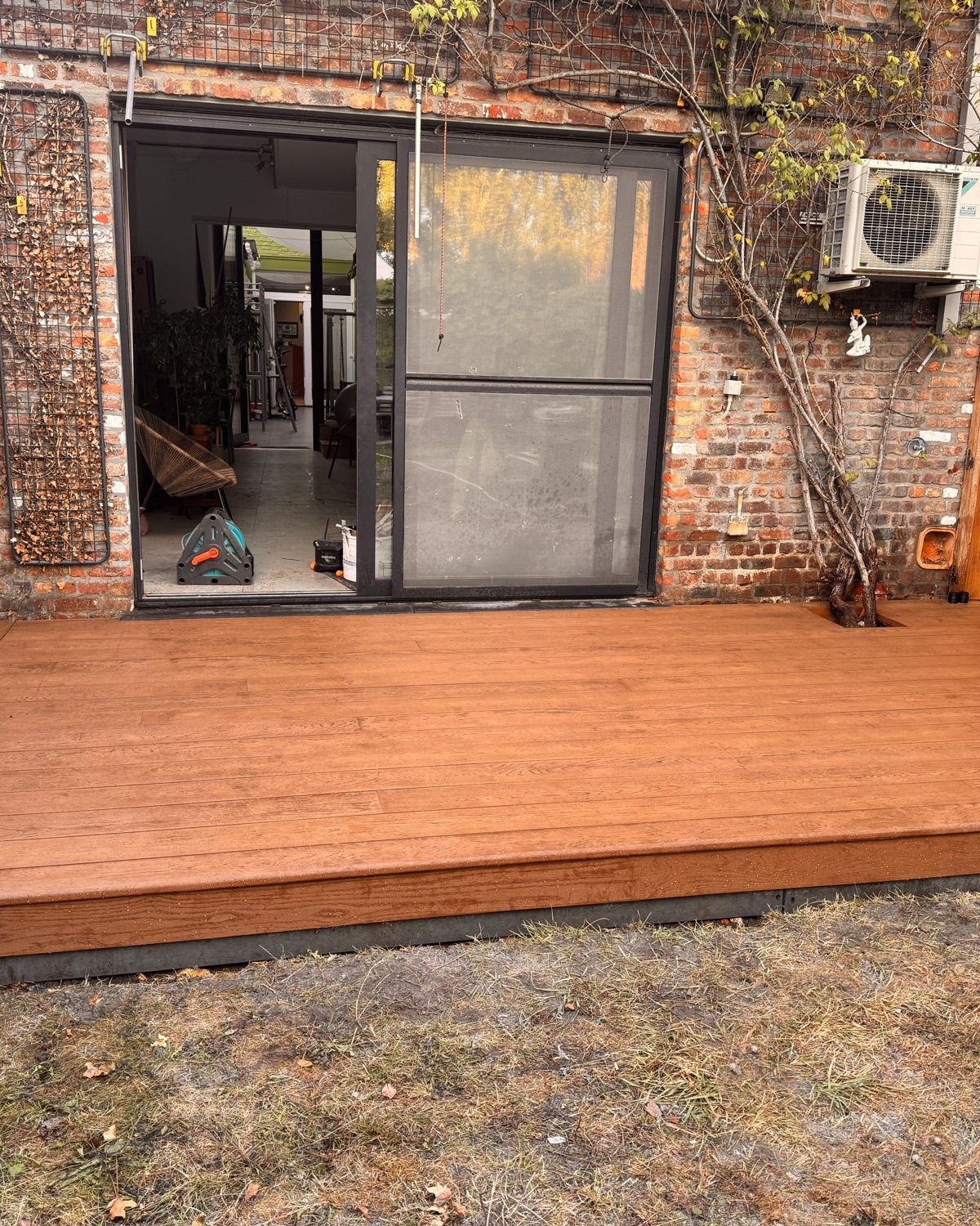 Afgewerkt terras in Millboard Enhanced Grain, kleur Coppered Oak, in de tuin voor het schuifraam van een bakstenen woning