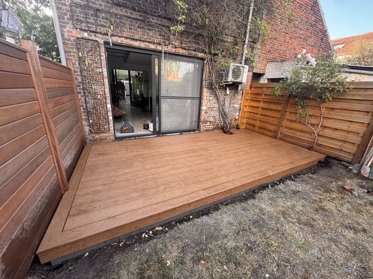 Afgewerkt terras in Millboard Enhanced Grain, kleur Coppered Oak, in een tuin met houten afsluitingen, schuin gezien vanaf de woning