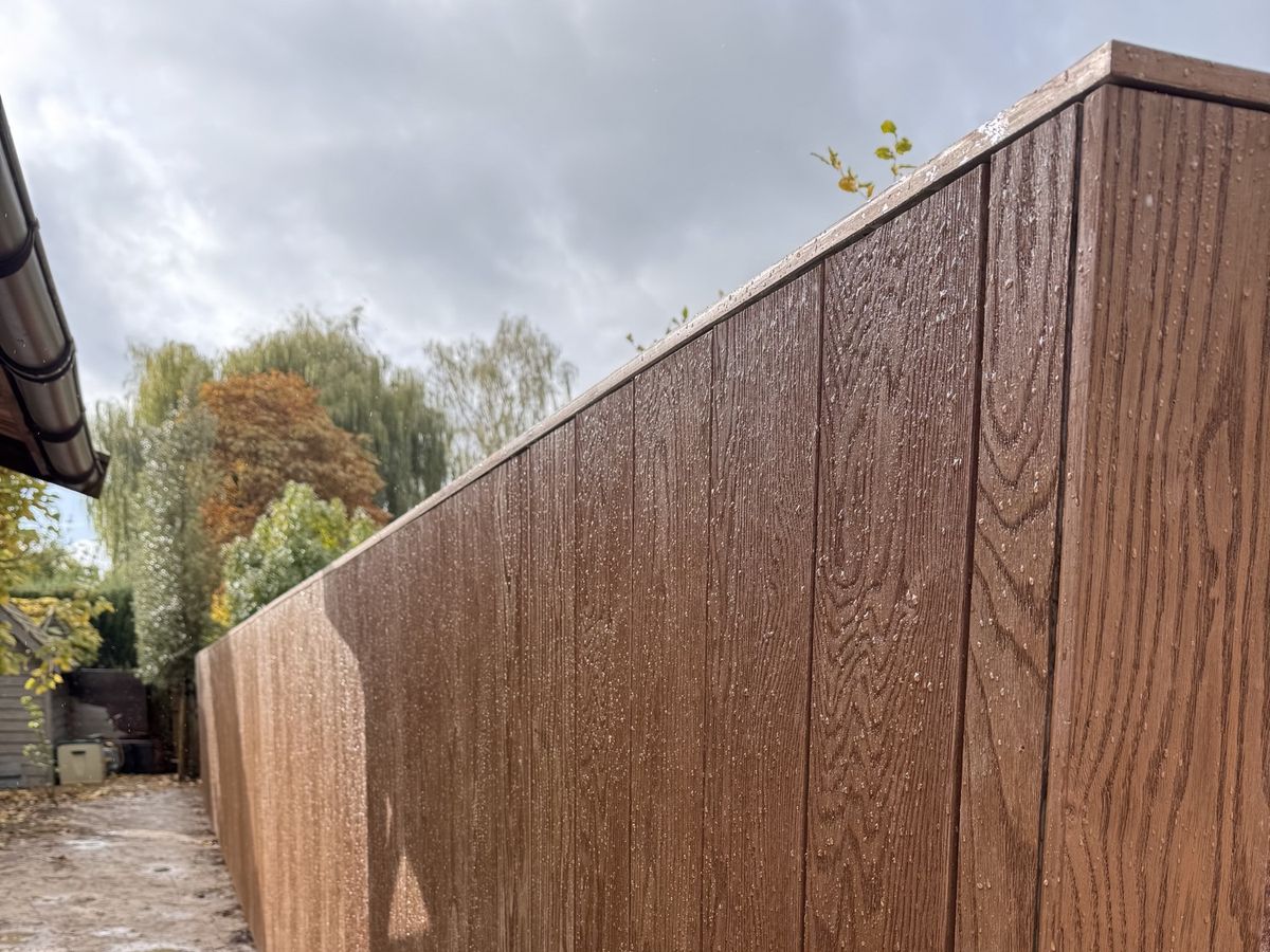 Tuinwand in Millboard-planken met een echte houtlook en een strakke afdeklijst, langs de rand van de tuin